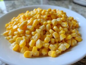 Close-up of a white plate piled high with creamy, glazed honey butter corn kernels.