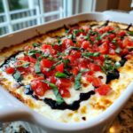 Close-up of a hot, baked bruschetta dip topped with diced tomatoes, fresh basil, and a balsamic glaze drizzle.