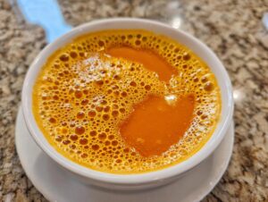 Close-up of hot, vibrant orange beer cheese dip with a foamy top, served in a white bowl.