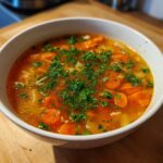 Close-up of a white bowl filled with vibrant Italian penicillin soup featuring sliced carrots and topped with fresh chopped parsley.