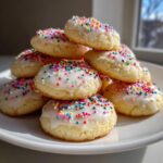 A tempting stack of soft Italian ricotta cookies topped with white glaze and colorful rainbow sprinkles.