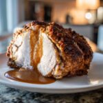 A close-up of a slice of juicy crockpot turkey roast, seasoned and covered in brown gravy on a white plate.