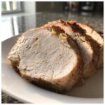 Close-up of thick, juicy slices of cooked slow cooker turkey breast on a white plate.