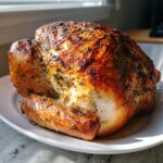 A whole roasted turkey with golden brown, herb-crusted skin resting on a white platter.