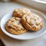 Three soft, crinkled maple brown sugar cookies drizzled with a white glaze, served on a white plate.