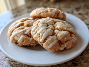 Three soft maple brown sugar cookies drizzled with white glaze, resting on a white plate.