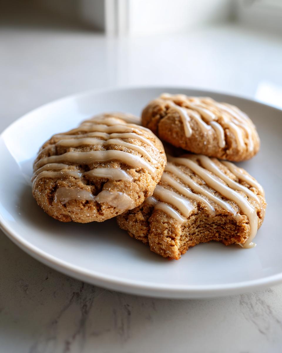 Three soft maple brown sugar cookies drizzled with glaze, one cookie has a bite taken out.