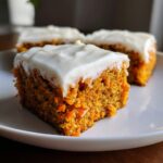 A close-up of a moist square of carrot cake bars topped with thick cream cheese frosting.