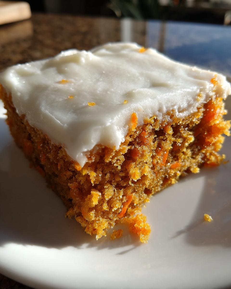 A close-up shot of a square piece of moist carrot cake bars topped with thick, white cream cheese frosting.