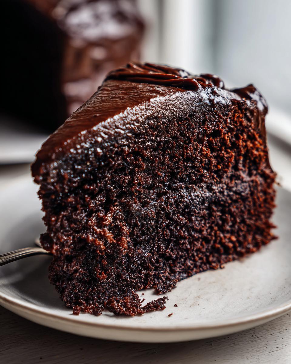 Close-up of a rich slice of moist chocolate cake topped with glossy dark chocolate frosting.