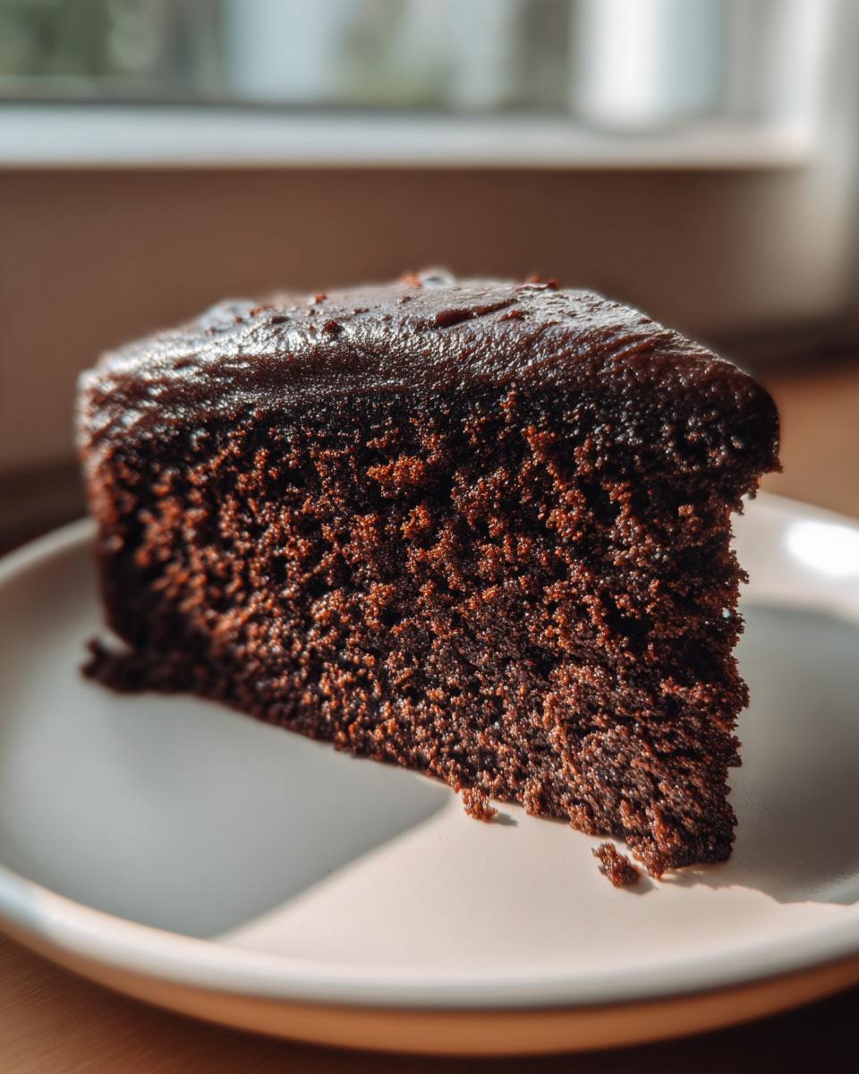 Close-up of a perfectly baked slice of moist chocolate cake topped with dark, glossy frosting.