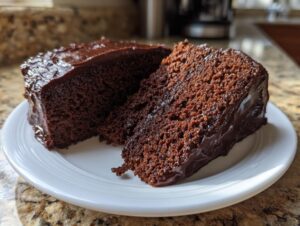A slice of incredibly moist chocolate cake with rich, glossy chocolate frosting on a white plate.