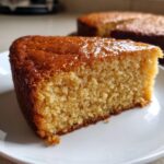 Close-up of a moist slice of golden condensed milk cake with a shiny glaze on a white plate.