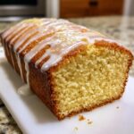 Close-up of a moist lemon pound cake loaf with a thick, drizzled white glaze and lemon zest topping.