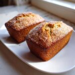 Two golden brown mini banana bread loaves sprinkled generously with coarse sugar, resting on a white plate.