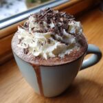 A close-up of a mug filled with rich boozy hot chocolate, topped with whipped cream and chocolate shavings.