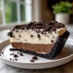 A decadent slice of no bake Oreo pie featuring a dark crust, chocolate layer, vanilla layer, and crumbled Oreo topping.