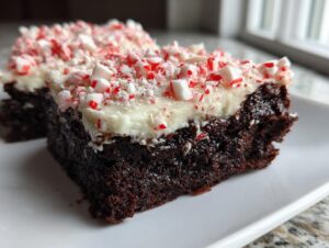 Close-up of rich, dark peppermint brownies topped with white frosting and crushed candy canes.