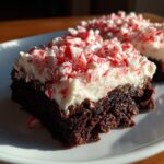 A rich, dark chocolate peppermint brownie slice topped with thick white frosting and crushed candy canes.