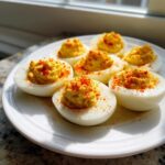 Six perfectly prepared deviled eggs arranged on a white plate, topped with creamy yolk filling and sprinkled with paprika.