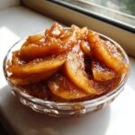 Close-up of sweet, spiced apple pie filling recipe slices in a small glass bowl by a window.