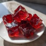 Close-up of bright red, glassy chunks of homemade cinnamon rock candy resting on a small white plate.