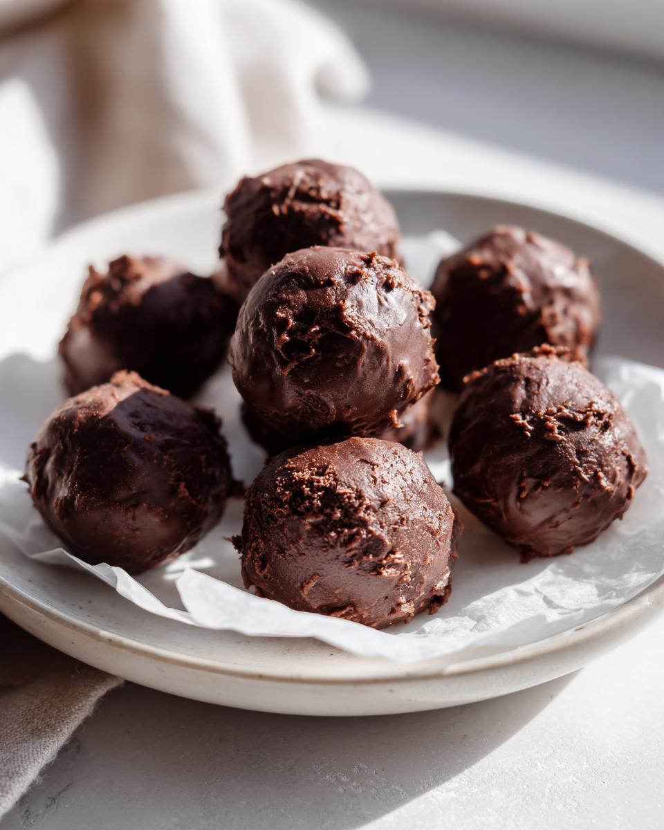 A pile of decadent, chocolate-coated oreo balls resting on white parchment paper on a light-colored plate.