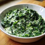Close-up of rich creamed spinach recipe, featuring dark green spinach coated in a creamy white sauce and topped with grated cheese.