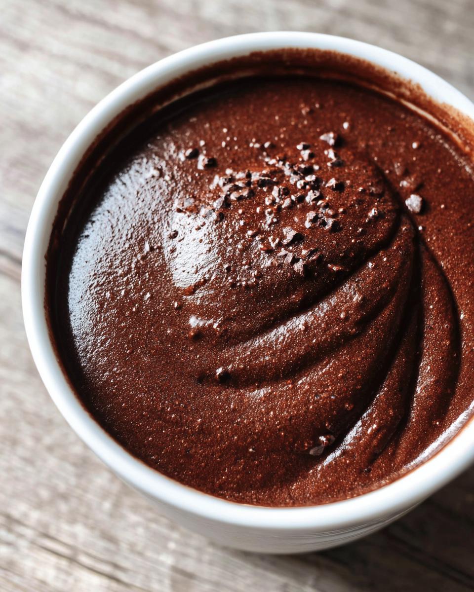Close-up of rich, dark homemade chocolate pudding topped with chocolate shavings in a white bowl.