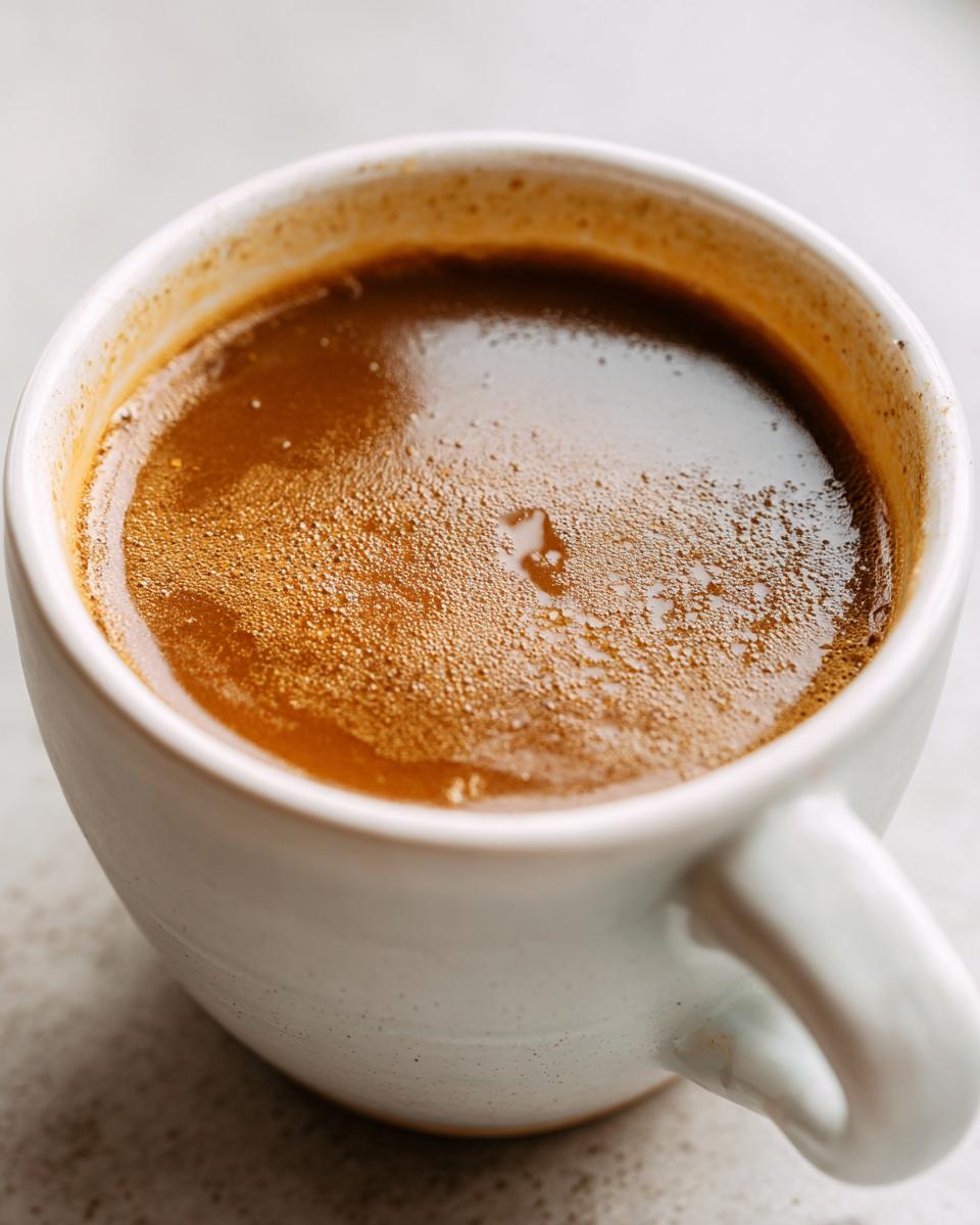 Close-up of rich, foamy brown turkey gravy in a white ceramic mug.