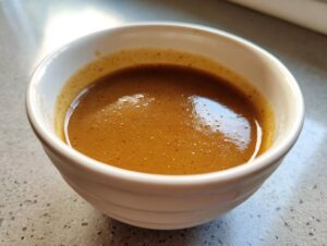 Close-up of rich, brown turkey gravy with a slight froth in a small white bowl.