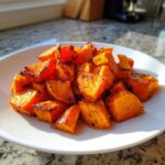 A white plate piled high with perfectly seasoned, caramelized roasted sweet potatoes cubes.