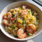 A close-up of shrimp cauliflower fried rice mixed with scrambled egg and green onions in a white bowl.