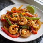 Close-up of seasoned shrimp fajitas with colorful bell peppers and onions, garnished with a lime wedge.