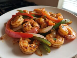 Close-up of seasoned shrimp fajitas mixed with sautéed red, green, and orange bell peppers and onions on a white plate.