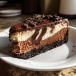 A decadent slice of 3 layer chocolate cheesecake featuring dark crust, marbled filling, and chocolate ganache topping.