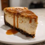 A close-up of a rich slice of biscoff cheesecake topped with a thick caramel sauce drizzle.