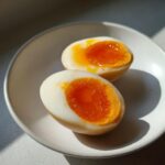 Two halves of soft-boiled marinated eggs showing jammy, bright orange yolks on a light plate.