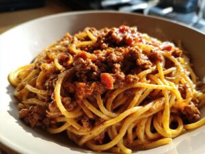 Close-up of spaghetti noodles generously coated in a rich, hearty bolognese sauce in a light-colored bowl.