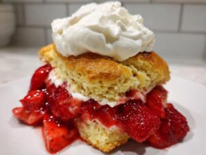A close-up of a delicious strawberry shortcake slice layered with macerated strawberries and topped with whipped cream.