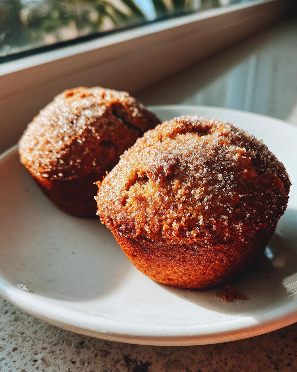Two golden brown mini banana bread loaves topped with sparkling sugar crystals sitting on a white plate.