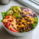 A close-up of a fresh cheeseburger bowl featuring seasoned ground beef, lettuce, tomatoes, pickles, red onion, and a drizzle of special sauce.