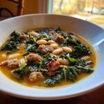 Close-up of a bowl of Tuscan white bean soup featuring cannellini beans, crumbled sausage, and dark green kale.
