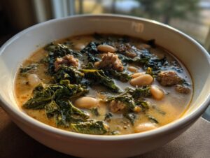 Close-up of a bowl of creamy Tuscan white bean soup featuring kale and crumbled sausage.