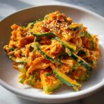 Close-up of a creamy, orange-hued kani salad mixed with sliced cucumbers and topped with sesame seeds.