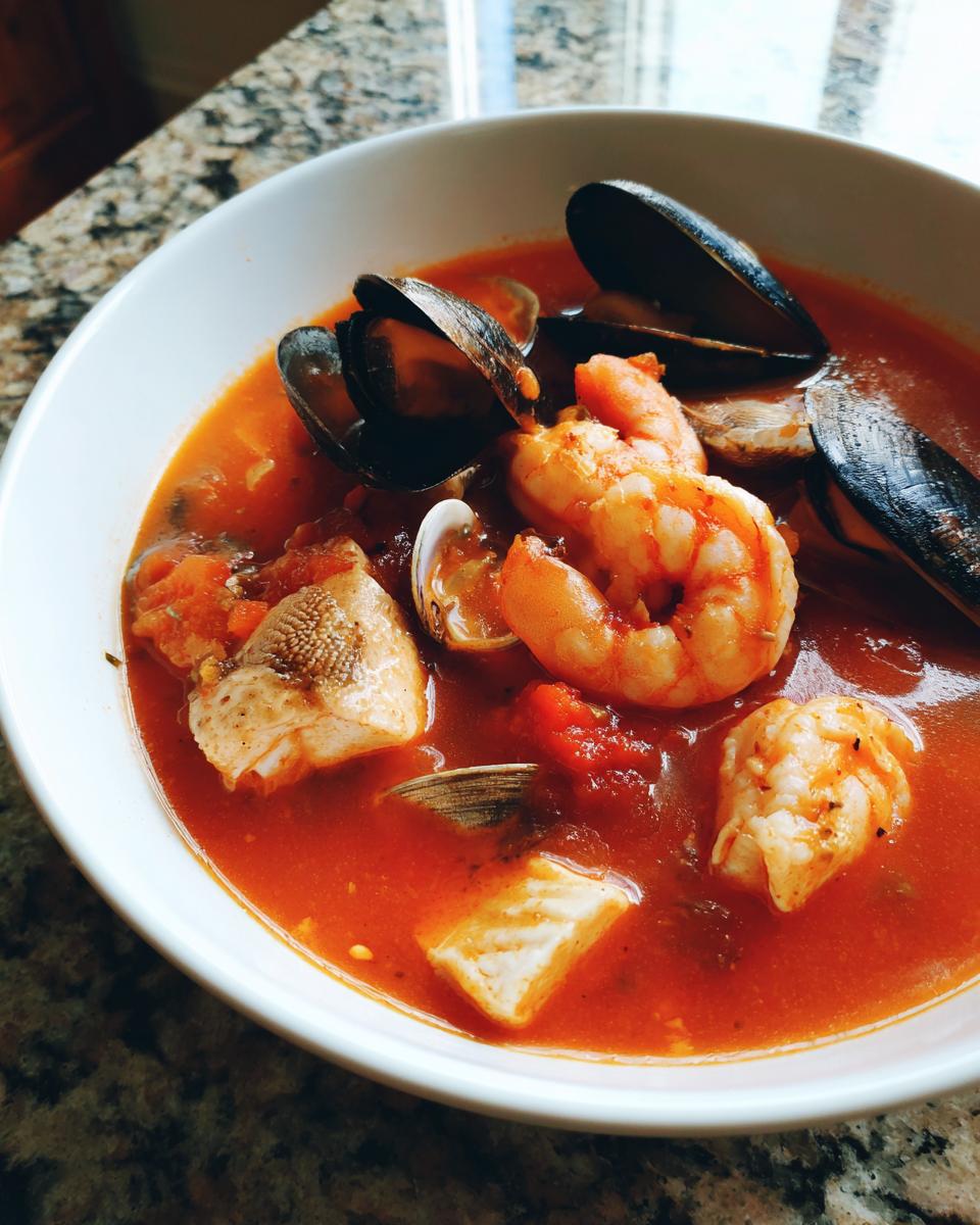 A close-up of a vibrant red seafood soup filled with shrimp, mussels, clams, and chunks of white fish.