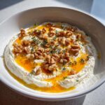 Close-up of a bowl of creamy whipped ricotta dip with hot honey, walnuts, and fresh thyme.