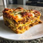 A thick, layered slice of zucchini lasagna showing meat sauce, cheese, and green zucchini noodles.