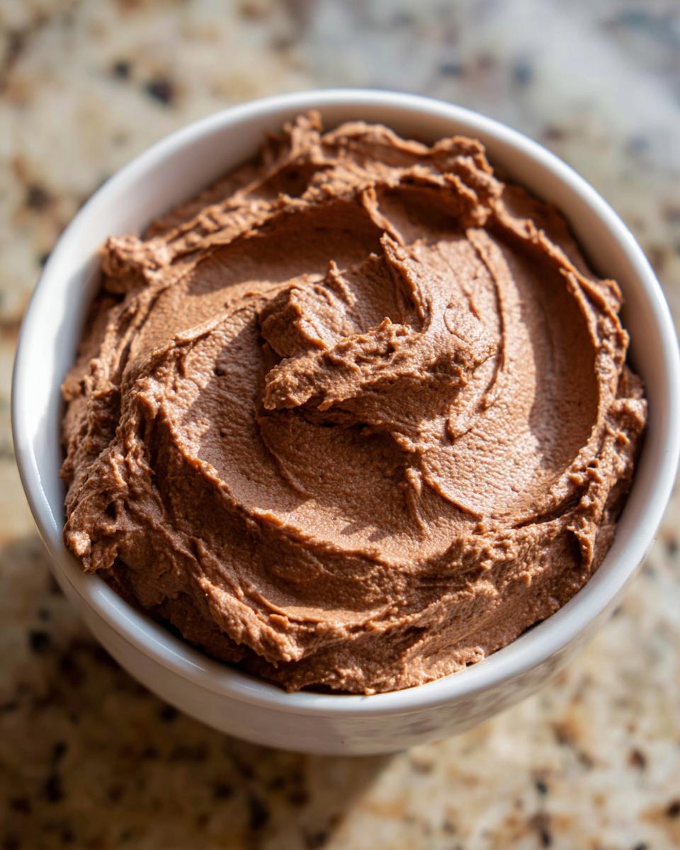 A close-up overhead shot of thick, swirled, rich brown 3-ingredient chocolate dip in a white bowl.