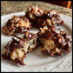 Close-up of an almond joy cookie broken in half showing coconut filling, topped with chocolate and almonds.